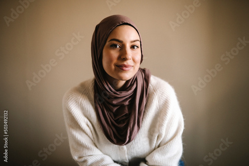 Smiling young woman in hijab against beige background photo