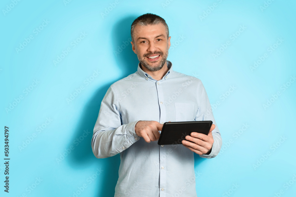 Middle Aged Man Using Tablet Browsing Internet On Blue Background Middle Aged Man Using Tablet Browsing Internet On Blue Background