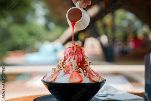 Japanese shaved ice dessert , Hand pouring sweet strawberry sauce on ice cream. Served with strawberry kakigori bingsu topped with almond stick condensed milk. Traditional summer dessert in Japan.
