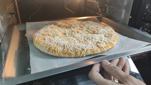 Hands are holding a tray with pizza and put it in the oven.