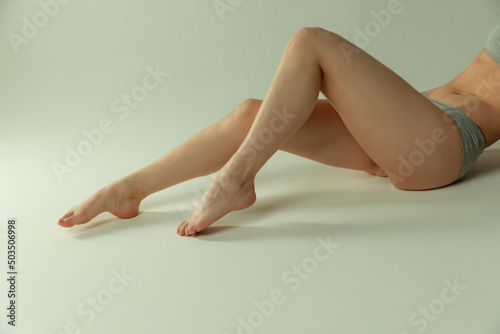 Beautiful slender female legs in gray underwear, laying over grey background. Depilation and epilation concept
