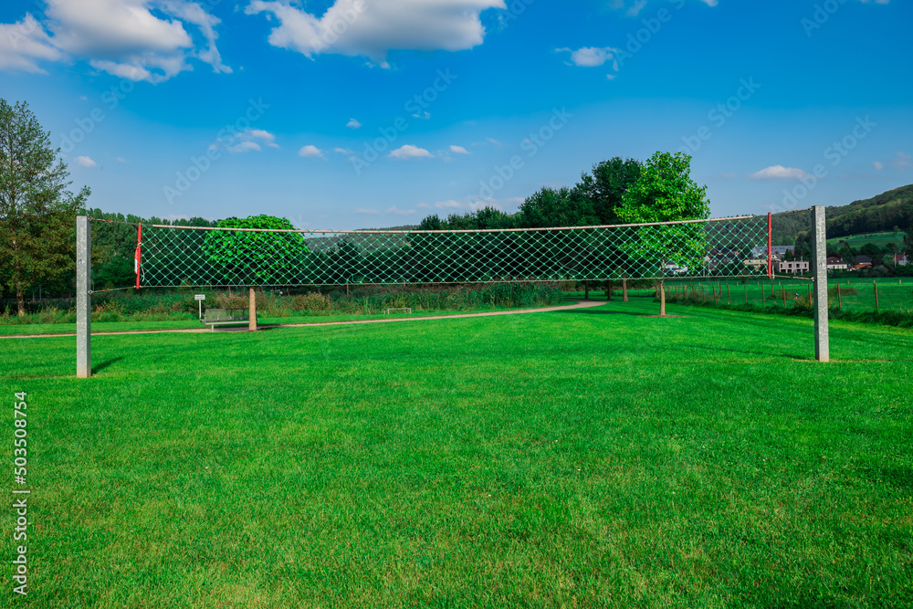 a volleyball court in a park. grass volleyball court. play sports outdoors. a volleyball net in the middle of a park with a blue sky