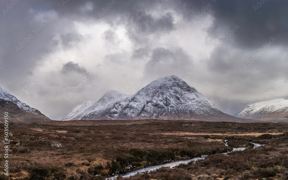 Beautiful Winter landscape image of Stob Dearg Buachaille Etive Mor viewed from Rannoch Moor with snowcapped peak and beautiful moody cloud formations