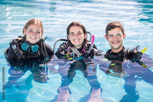 A group of happy scuba divers standing in a pool with their gear on smiling at the camera