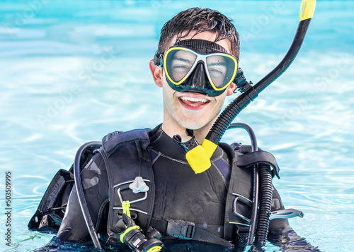 A happy young man with scuba gear on in a pool smiling at the camera