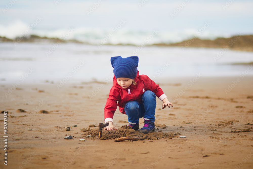 Adorable toddler girl playing on the sand beach at Atlantic coast of Zumaia, Basque Country, Spain Adorable toddler girl playing on the sand beach at Atlantic coast of Zumaia, Basque Country, Spain