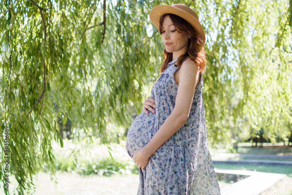 Pregnant woman outdoors in the park on a summer day. Place for text.
