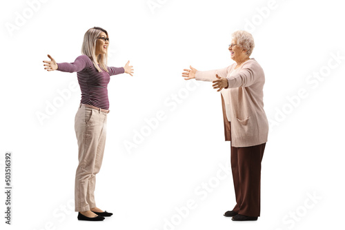 Full length profile shot of a young woman meeting an elderly woman with arms wide open