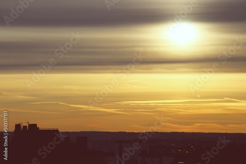 Atardecer dorado sobre la ciudad de Madrid en España. El sol tras unas frías nubes de finales de otoño creando un efecto distorsionador sobre la silueta del sol y el horizonte.