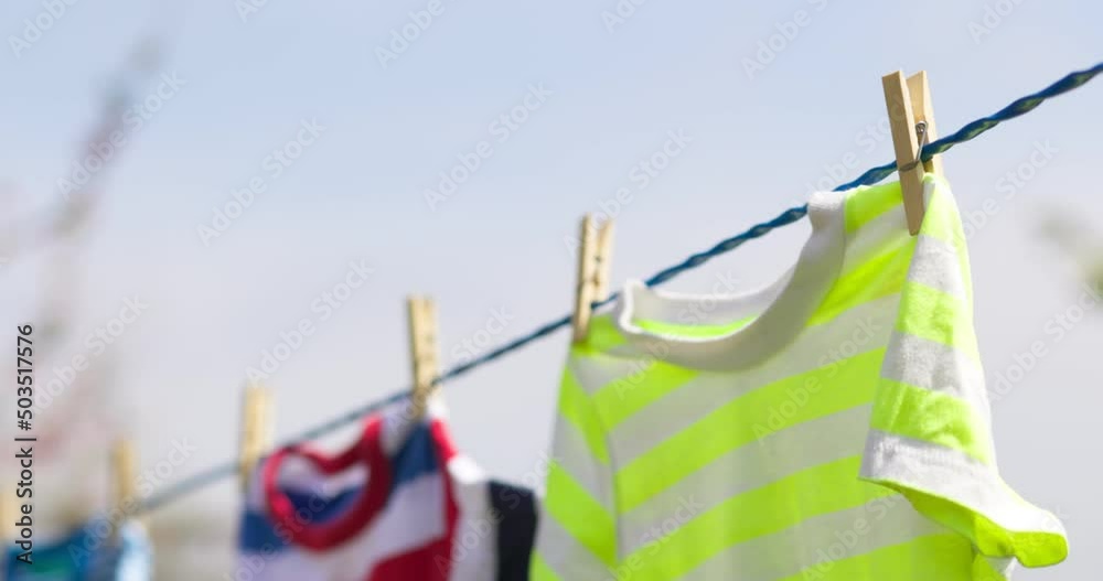 Clean clothes on rope outdoors on laundry day. Colorful t-shirts hanging on a laundry line against blue sky