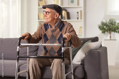 Fotografie Elderly man sitting on a sofa and holding onto a walker