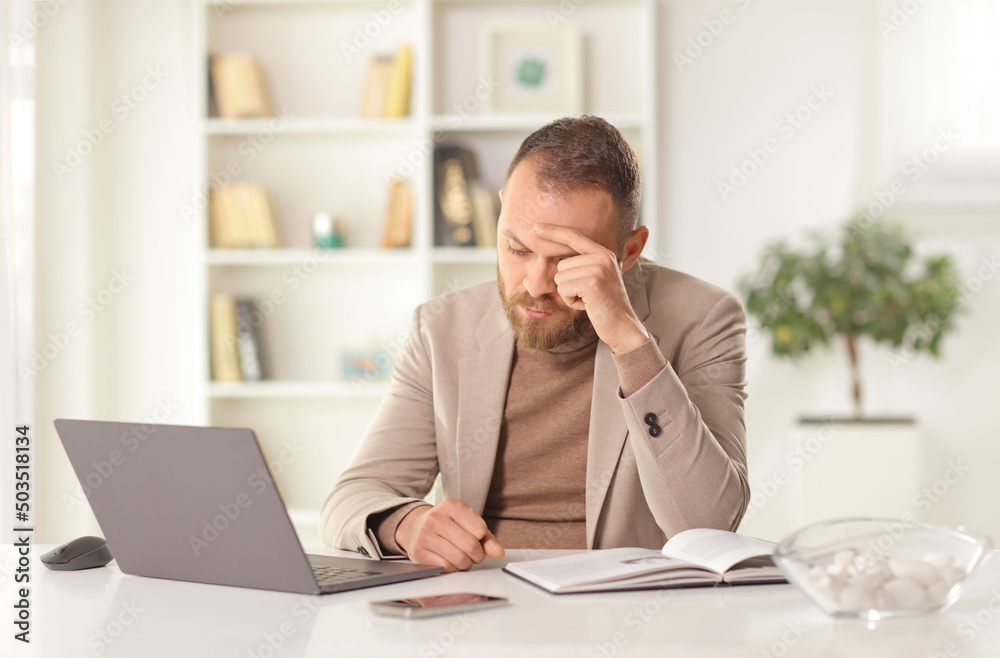Tired young man working from home with a laptop computer sitting and holding his head Tired young man working from home with a laptop computer sitting and holding his head
