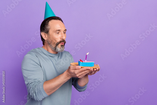 Profile side photo of mature man blow candle dreamy delicious dessert isolated over violet color background