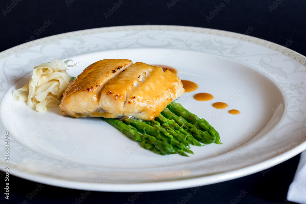 morue grill with asparagus and ginger on white plate on dark table morue grill with asparagus and ginger on white plate on dark table