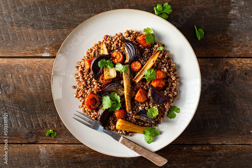 Buckwheat salad with roasted root vegetables. Rustic wooden table.