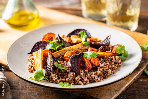 Buckwheat salad with roasted root vegetables. Rustic wooden table.