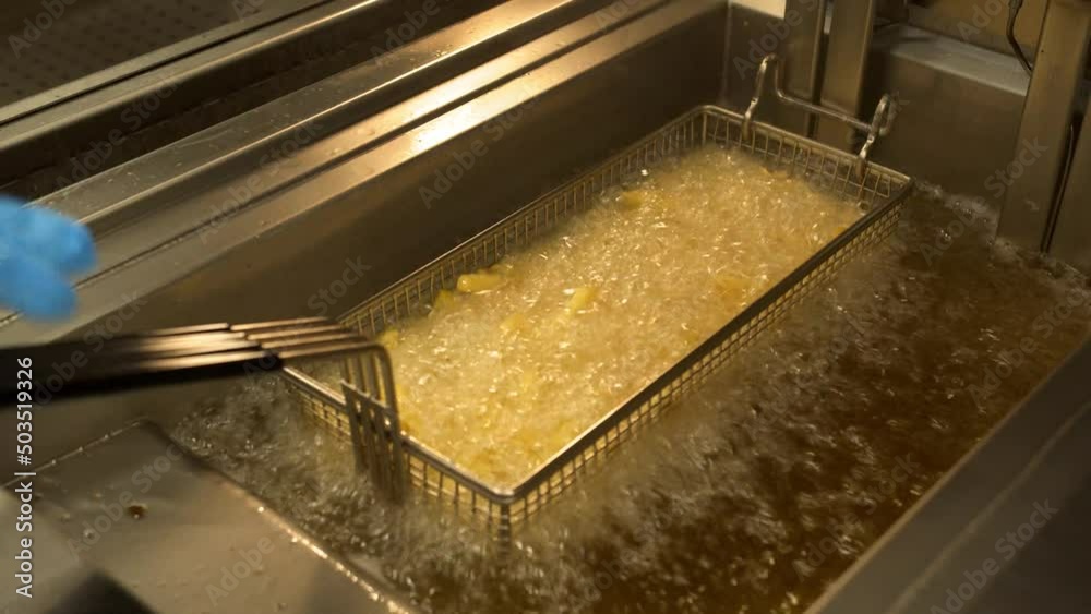Close up of french fries is cooking into deep fryer. Crunchy potatoes is frying in hot boiling oil at cuisine. Process of making fast food at kitchen. Food preparing concept. Top view Slow motion