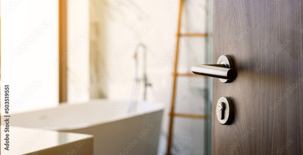 wooden door open to nice modern bathroom, marble walls. selective focus to door handle, bathroom and bathtub blurred on background. - obrazy, fototapety, plakaty 