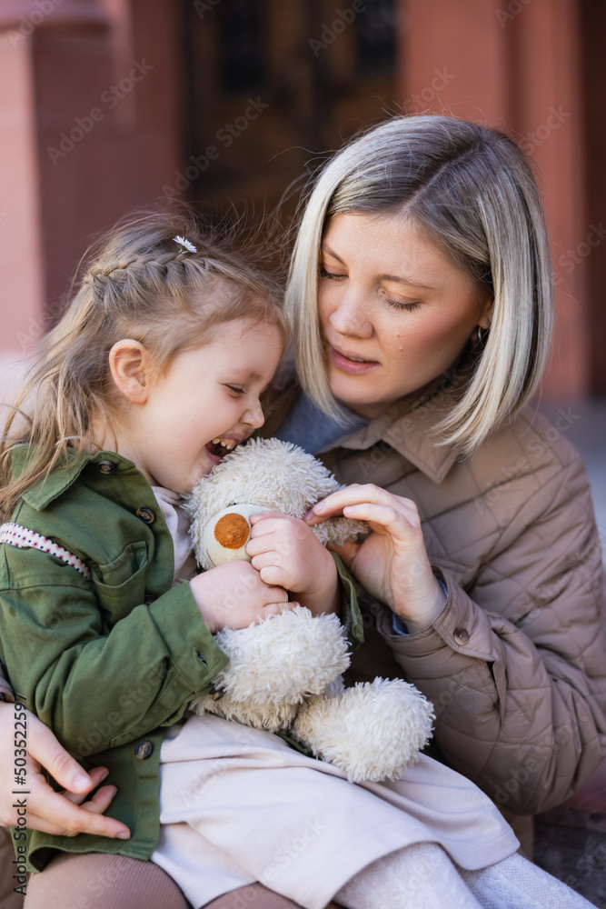 excited girl holding teddy bear near mother outdoors. excited girl holding teddy bear near mother outdoors.