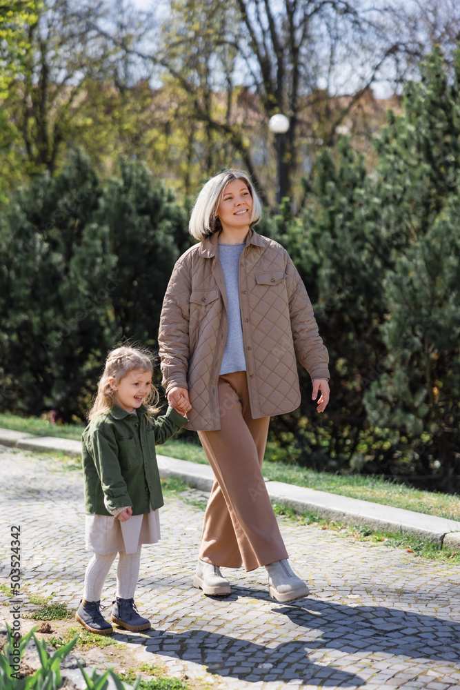 Obraz premium full length of happy and stylish woman with daughter walking in spring park.