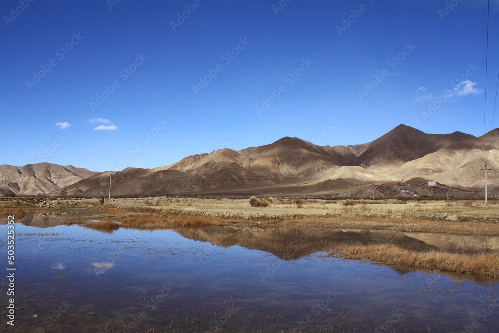 andscape between Tibet to Shigatse  Tibet China.The rock mountains range ,dried grasses reflection in the lake with blue sky