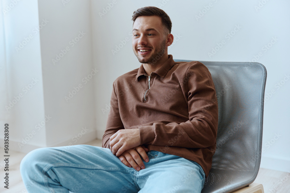 Cheerful smiling happy young tanned man fold hands looks aside dreaming about holiday plans cool idea for startup have insight siting in chair at home. People emotions concept. Copy space