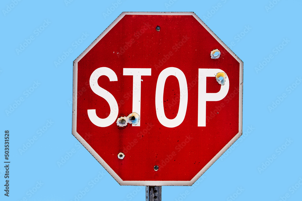 Grungy stop sign shot full of bullet holes isolated on sky blue - room for text