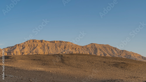 A picturesque rock devoid of vegetation against a clear blue sky. In the foreground is a desert sand dune. Egypt. Luxor.