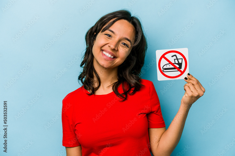 Young hispanic woman holding no eating sign isolated on blue background happy, smiling and cheerful. Young hispanic woman holding no eating sign isolated on blue background happy, smiling and cheerful.