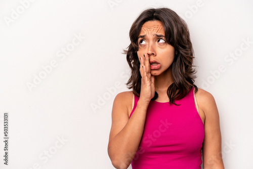 Young hispanic woman isolated on white background is saying a secret hot braking news and looking aside