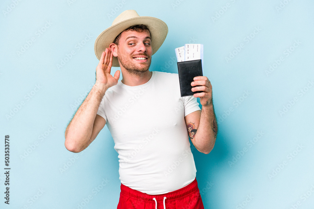 Young caucasian traveler man holding passport isolated on blue background trying to listening a gossip. Young caucasian traveler man holding passport isolated on blue background trying to listening a gossip.
