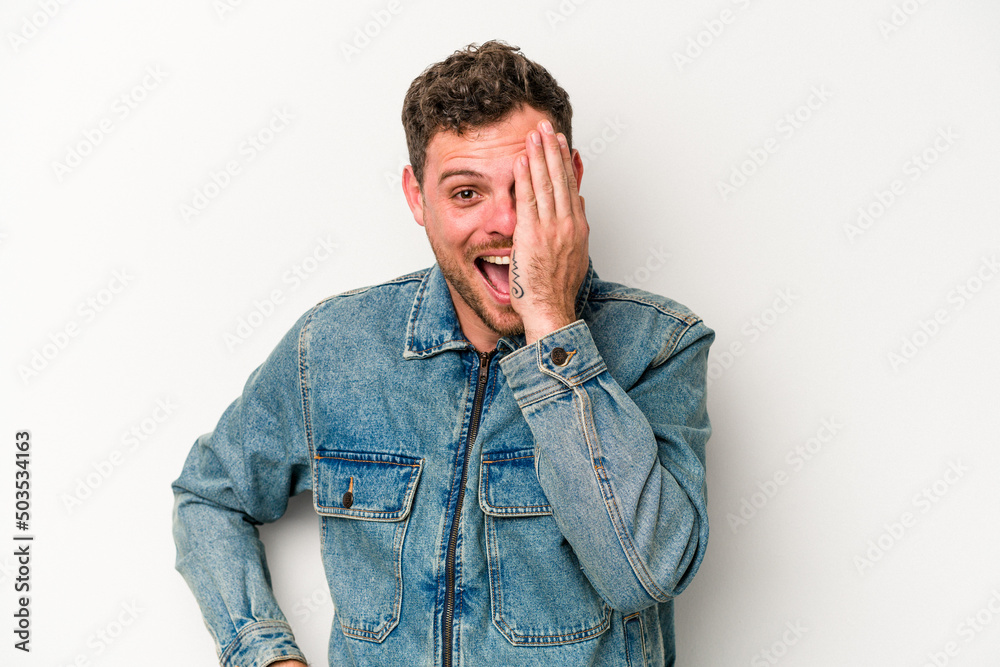 Young caucasian man isolated on white background having fun covering half of face with palm.