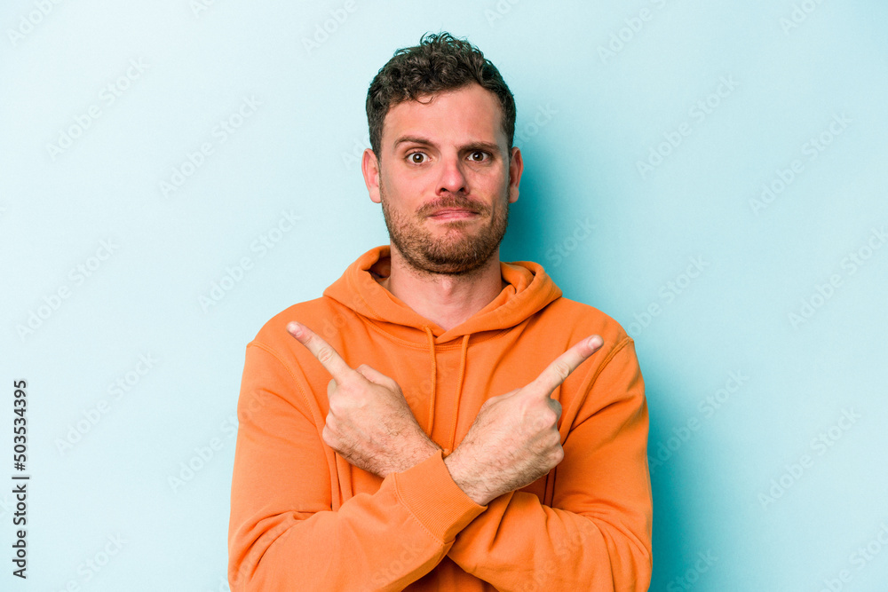 Young caucasian man isolated on blue background points sideways, is trying to choose between two options.