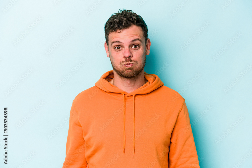 Young caucasian man isolated on blue background blows cheeks, has tired expression. Facial expression concept. Young caucasian man isolated on blue background blows cheeks, has tired expression. Facial expression concept.