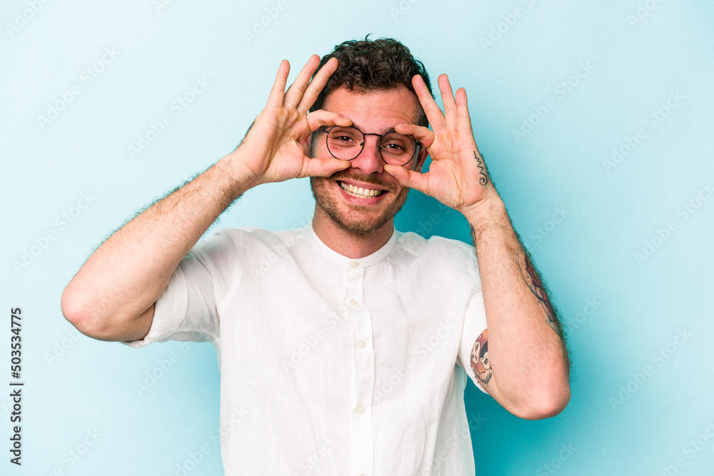 Young caucasian man isolated on blue background excited keeping ok gesture on eye. Young caucasian man isolated on blue background excited keeping ok gesture on eye.