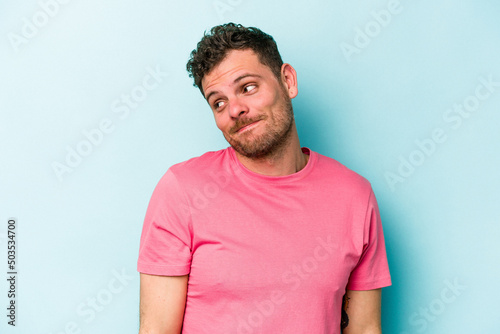 Young caucasian man isolated on blue background laughs and closes eyes, feels relaxed and happy.