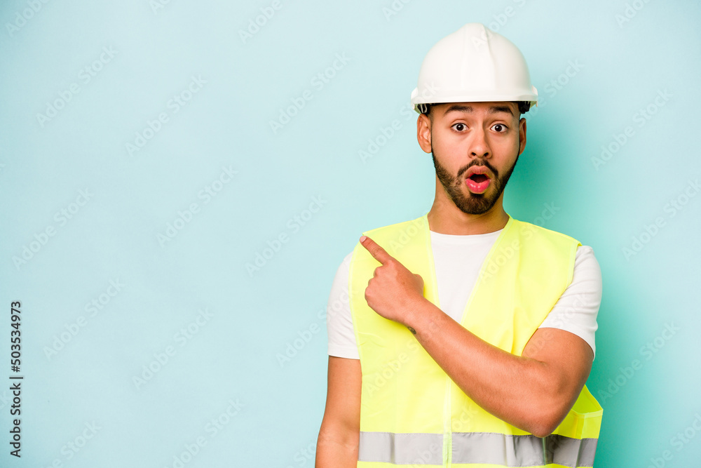 Young laborer hispanic man isolated on blue background pointing to the side