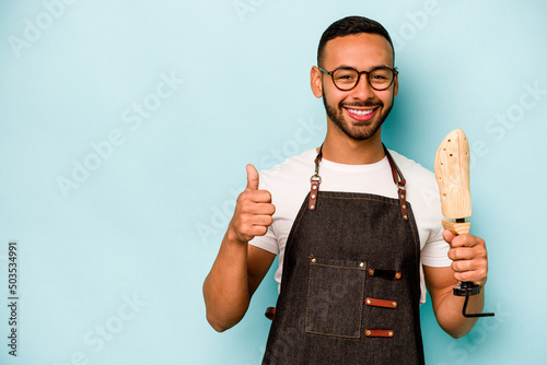 Young hispanic shoemaker man isolated on blue background smiling and raising thumb up photo