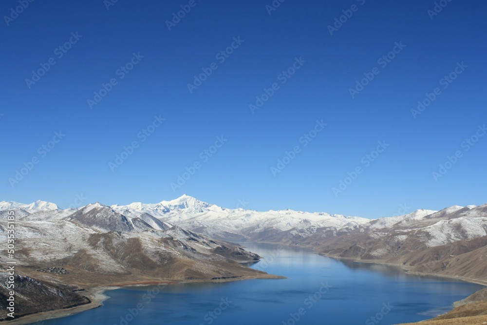 snow covered mountains Landscape of yamdrok   tso lake surround with snow capped mountains and bright blue sky Tibet China. the freshwater lake in Tibet