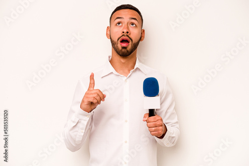 Young hispanic TV presenter isolated on blue background pointing upside with opened mouth.