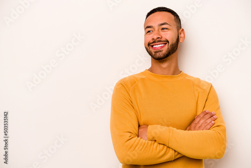 Young hispanic man isolated on white background smiling confident with crossed arms. © Asier