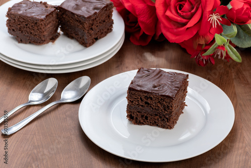 slice of chocolate cake covered with chocolate, served chilled, a bouquet of red roses next to the plate
