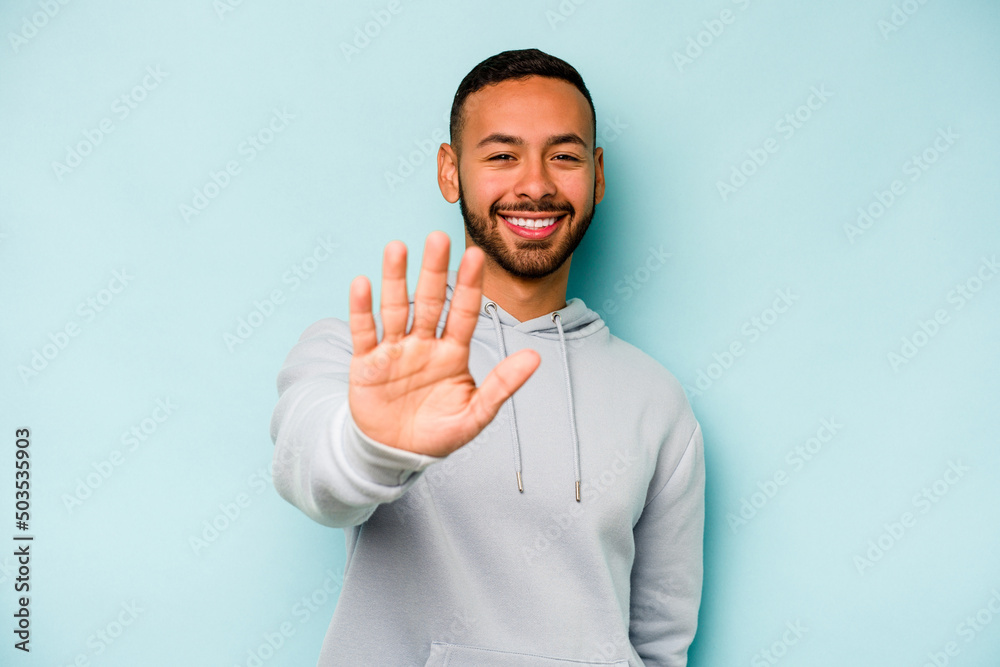 Young hispanic man isolated on blue background smiling cheerful showing number five with fingers. Young hispanic man isolated on blue background smiling cheerful showing number five with fingers.