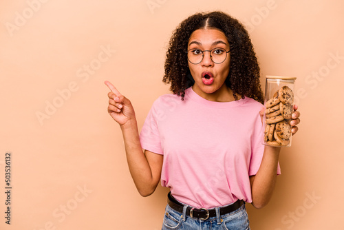 Fotobehang Young African american woman holding a cookies jar isolated on beige background