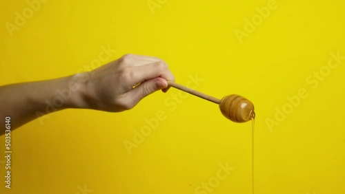 Female hands holding stick honey spoon on yellow background