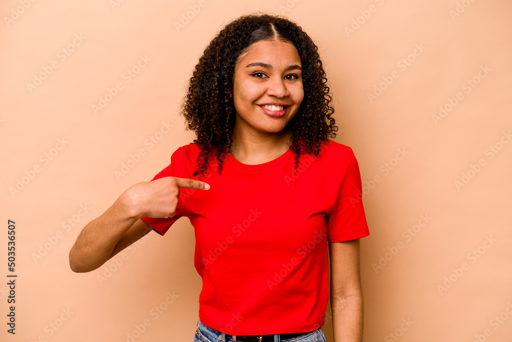 Young African American woman isolated on beige background person pointing by hand to a shirt copy space, proud and confident Young African American woman isolated on beige background person pointing by hand to a shirt copy space, proud and confident