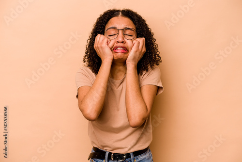 Young African American woman isolated on beige background crying, unhappy with something, agony and confusion concept.