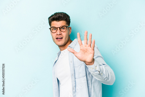 Young caucasian man isolated on blue background being shocked due to an imminent danger © Asier