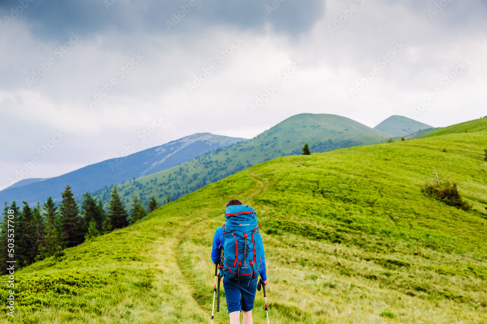 Obraz premium young man with backpack and trekking poles hiking in the mountains