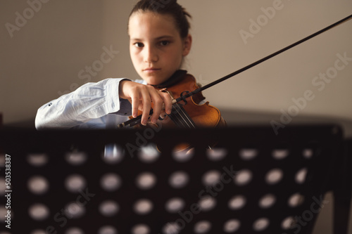 Teenager playing violin indoors. Teenage violinist student practicing at school, selective focus on his hand holding bow.
